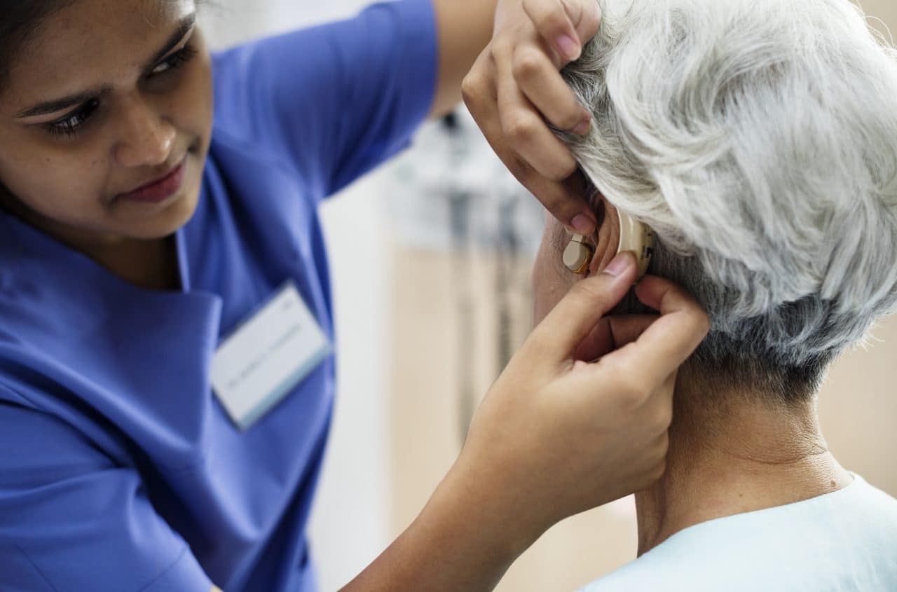 An audiologist fitting a woman with a new hearing aid.