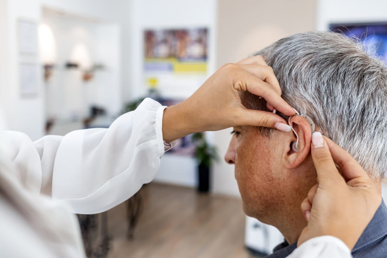 Mature man at medical examination or checkup in otolaryngologist's office. Doctor Fitting To Male Patient Hearing Aid.