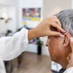 Mature man at medical examination or checkup in otolaryngologist's office. Doctor Fitting To Male Patient Hearing Aid.