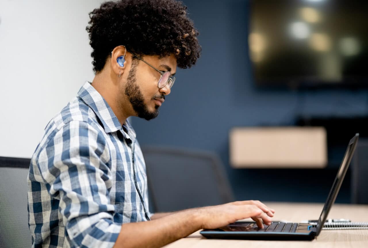 Man wearing hearing aids working on laptop at office