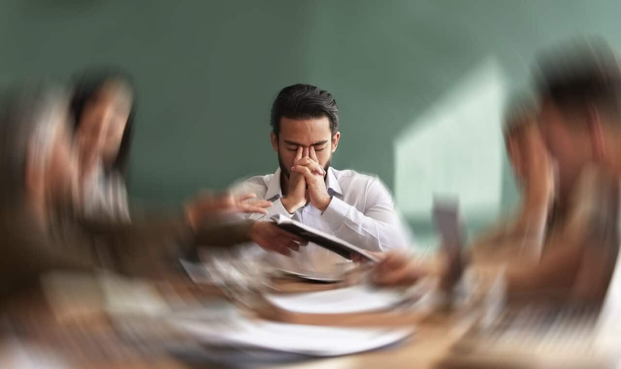 Man with stress tinnitus in a meeting holding his face.