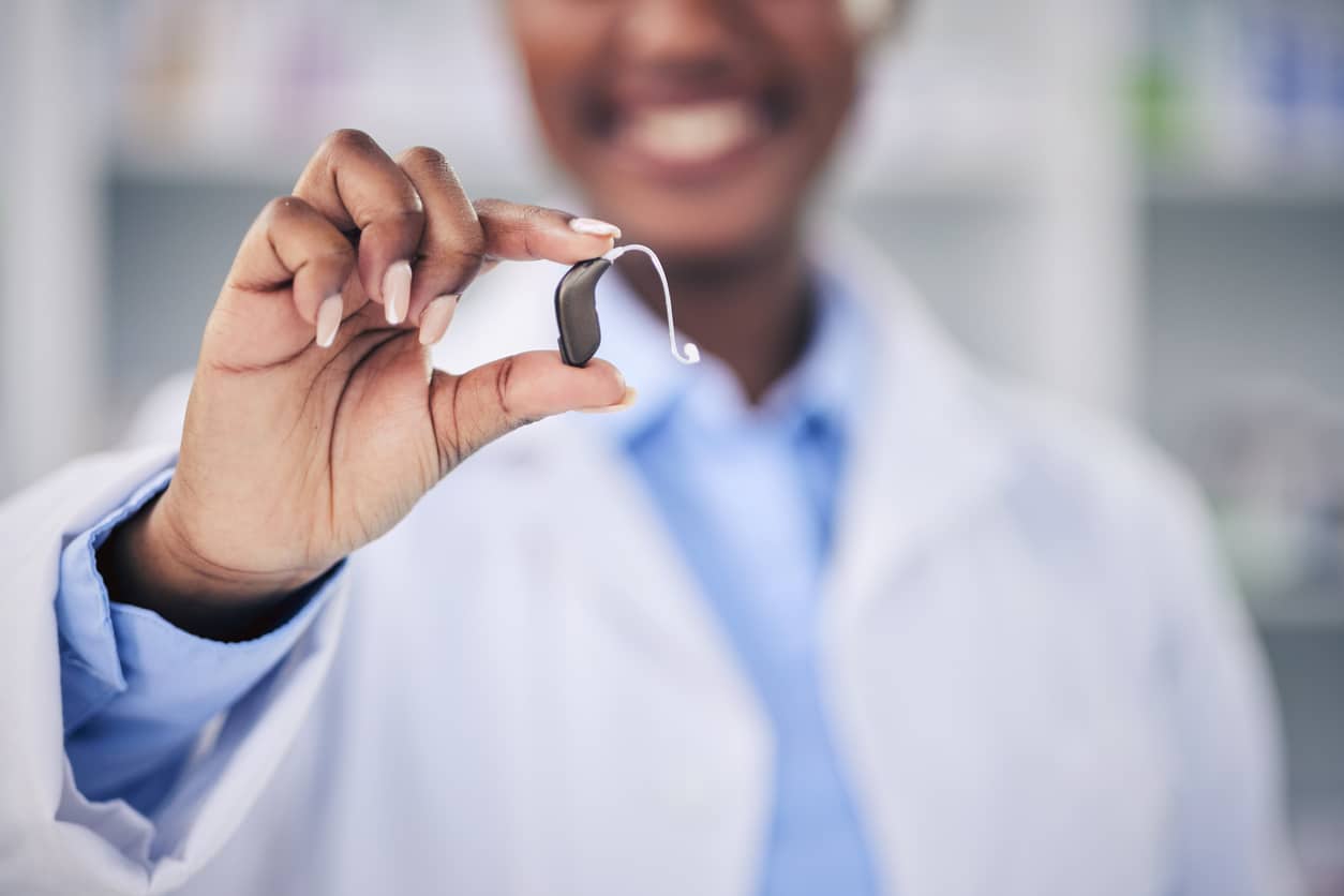 Smiling audiologist holds up a new top-of-the-line hearing aid